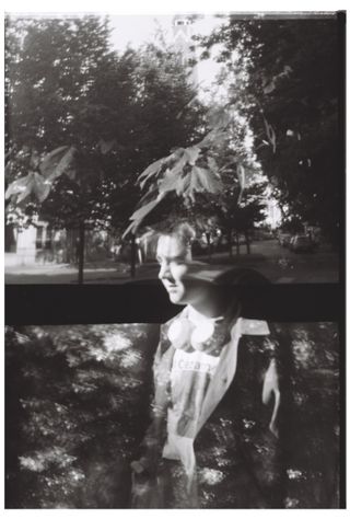 A black and white double exposure: a smiling person's face and shoulders blended with trees and leaves.