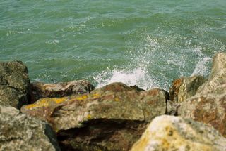Green-grey sea water splashing against lichen-covered rocks.